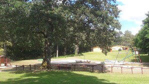 A park with a playground, a large tree, and a building in the background. - Cosy cottage in Sauzé-Vaussais with shared pool (SAUZE-VAUSSAIS)