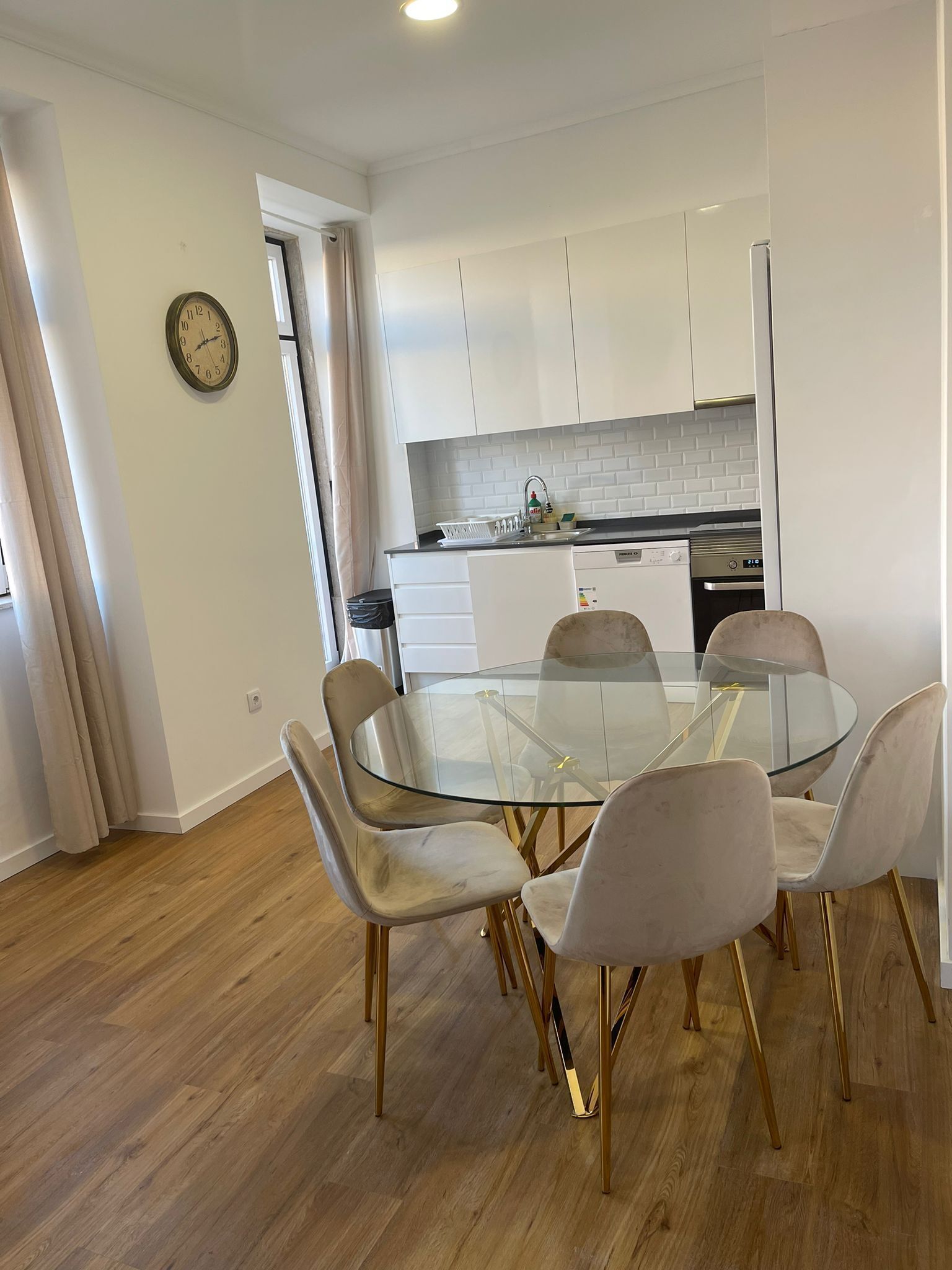 Une cuisine moderne avec des meubles blancs, une table à manger en verre et des chaises dorées.