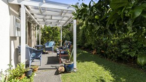 Un patio couvert aménagé avec du mobilier d’extérieur, une pergola et une végétation luxuriante.