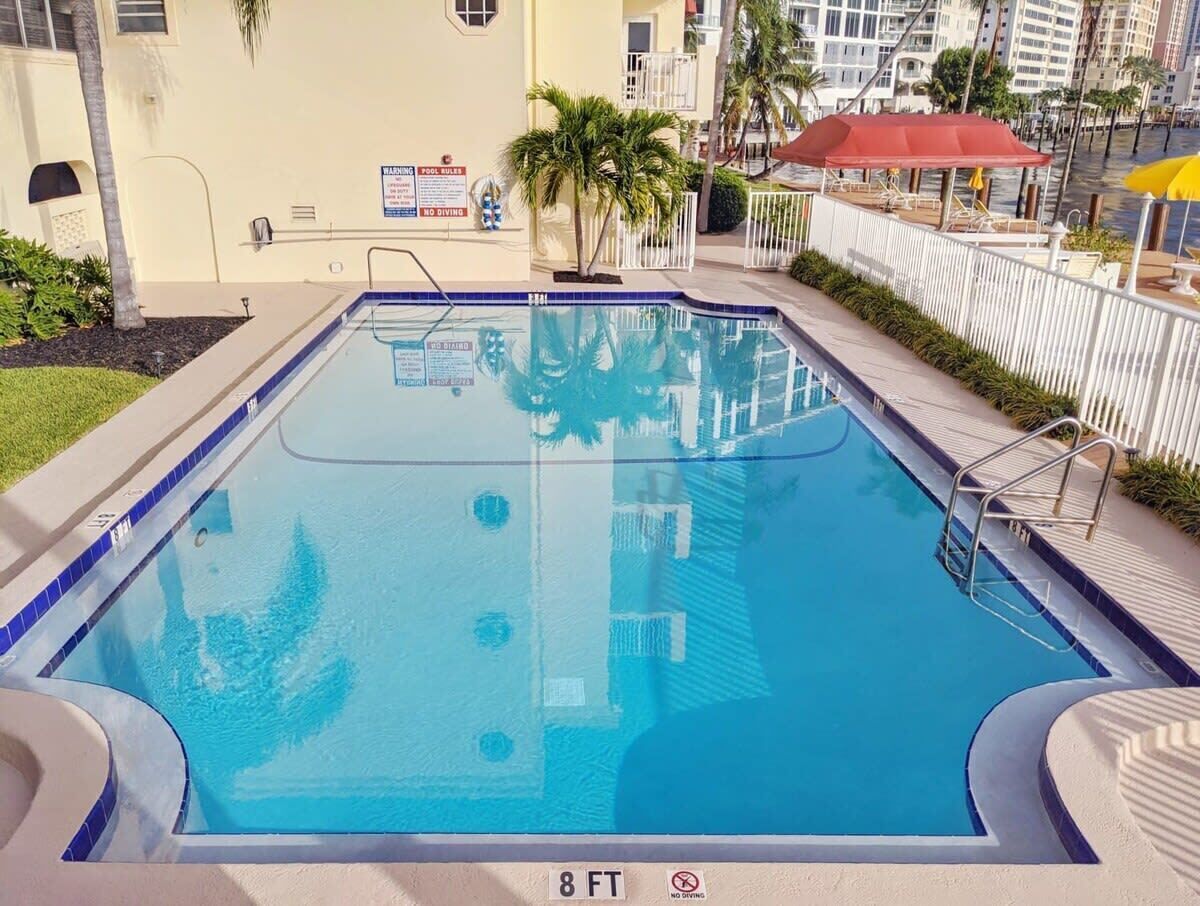 A rectangular swimming pool with a blue border, surrounded by a white fence, and a sign indicating a depth of 8 feet.