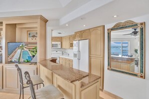 Une cuisine dotée de meubles en bois, d’un plan de travail en granit, d’un réfrigérateur en acier inoxydable et d’un grand miroir décoratif.
