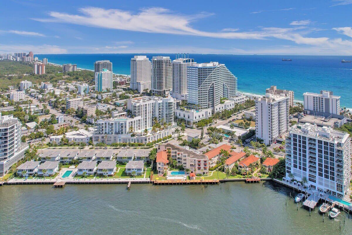 A coastal cityscape with high-rise buildings, a marina with boats, and a clear view of the ocean.