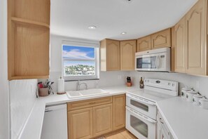 Uma cozinha moderna com bancadas brancas, armários de madeira, micro-ondas embutido e uma janela com vista para edifícios.