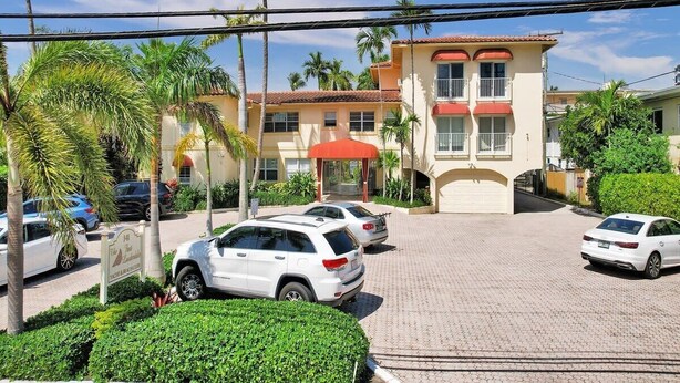 A hotel with a two-story building, a covered entrance, and a parking lot with several cars.