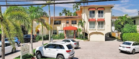 Un hotel con un edificio de dos pisos, un acceso cubierto y un estacionamiento con varios automóviles.