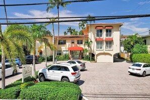 Un hotel con un edificio de dos pisos, un acceso cubierto y un estacionamiento con varios automóviles.