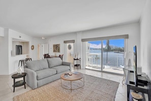 A modern living room with a grey sofa, a round coffee table, and a view of the sea through large windows.