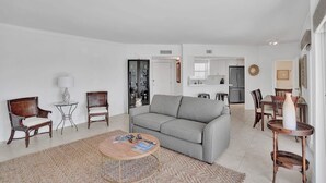 A living room with a grey sofa, two wicker chairs, a coffee table, and a dining area with a table and chairs.