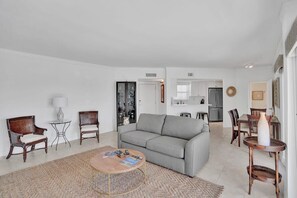 Una sala moderna con un sofá gris, dos sillones de mimbre, una mesa de centro y un comedor con mesa y sillas.