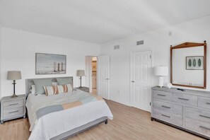 A bedroom with a bed, bedside tables, a dresser, a mirror, and a door.