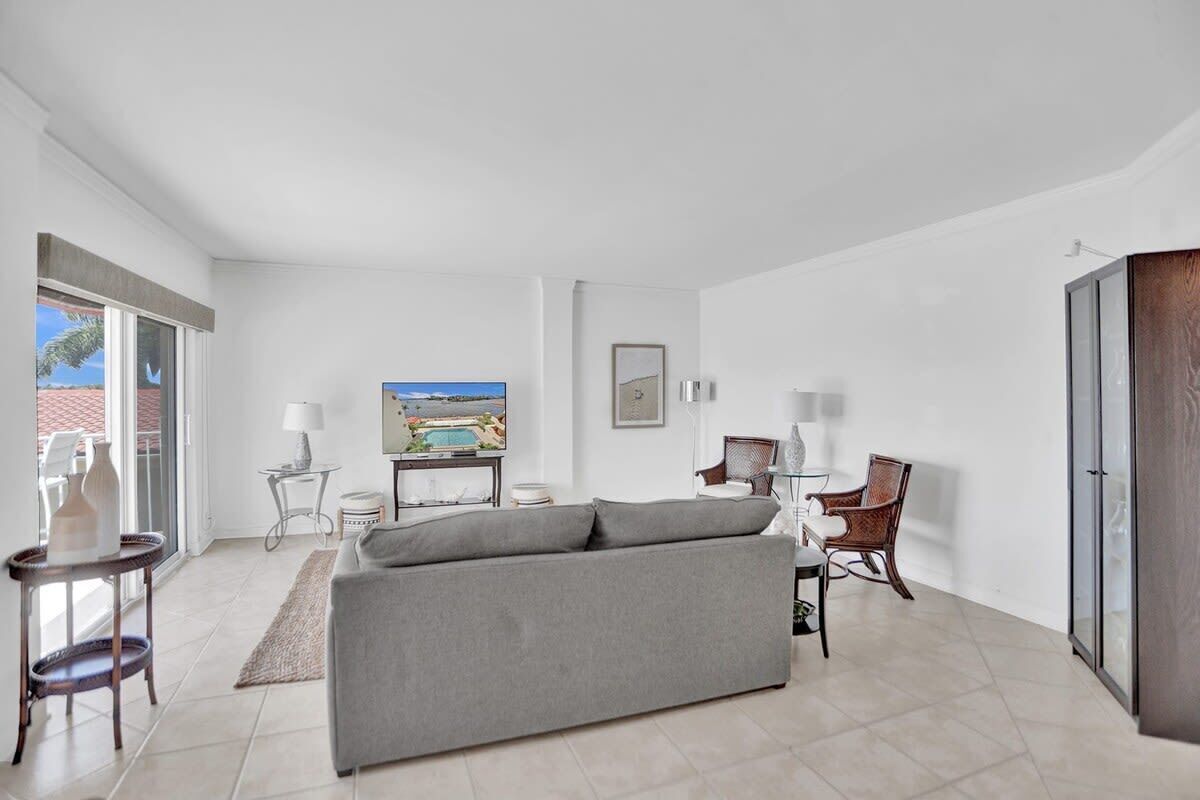 A modern living room with a grey sofa, a television, a small table with a lamp, and a chair.