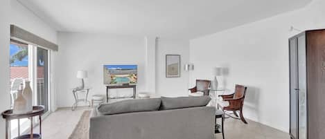A modern living room with a grey sofa, a television, a small table with a lamp, and a chair.