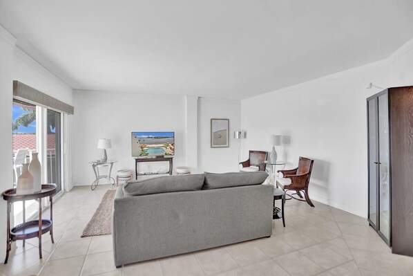 A modern living room with a grey sofa, a television, a small table with a lamp, and a chair.