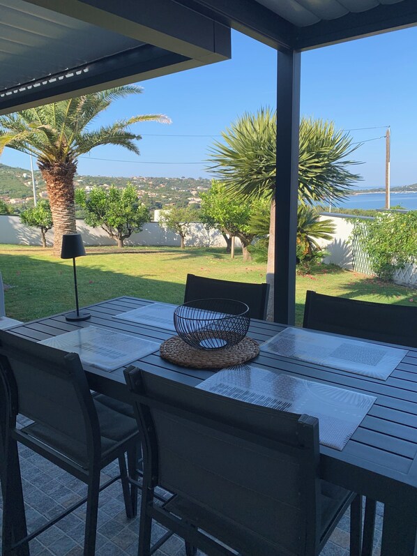 Un área de comedor al aire libre con una mesa, sillas y vistas al mar y vegetación.