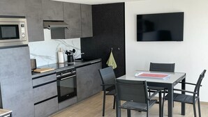 Una cocina moderna con microondas integrado, horno y cocina a gas. Hay una mesa de comedor con cuatro sillas y un televisor de pantalla plana montado en la pared.