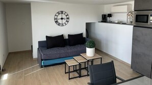 Una sala de estar moderna con un sofá, una mesa de centro, una silla negra, un reloj y una zona de cocina con microondas.