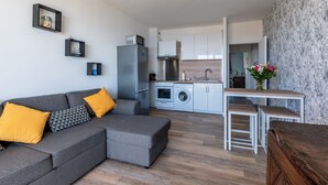 A modern apartment with a grey sectional sofa, a wooden dining table, a built-in kitchen with white cabinets, and a washing machine. - Chapelle des Grecs - 1km de la plage (Ajaccio)