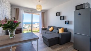 A modern living room with a grey sofa, a wooden dining table, and a refrigerator. - Chapelle des Grecs - 1km de la plage (Ajaccio)