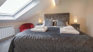 Une chambre à coucher avec un grand lit, un fauteuil rouge, deux tables de chevet avec des lampes, un radiateur et une lucarne.