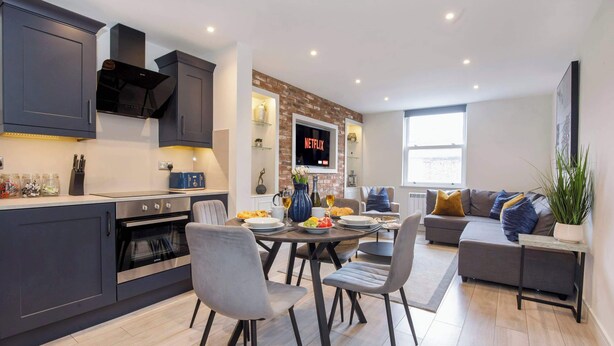 Une cuisine moderne avec des meubles de couleur sombre, un four encastré et un coin repas comprenant une table et des chaises.