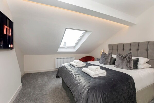 A modern bedroom with a skylight, a large bed, and a flat-screen TV displaying 'NETFLIX'.