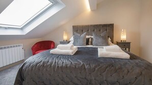 A bedroom with a large bed, a red chair, two bedside tables with lamps, and a skylight. - York Luxury Apt: Bishopthorpe Rd 2, Sleeps 6 (York)