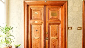 A wooden double door with plaques, a potted plant, and a doormat. - Rometobe Rooms & Hospitality (Rome)