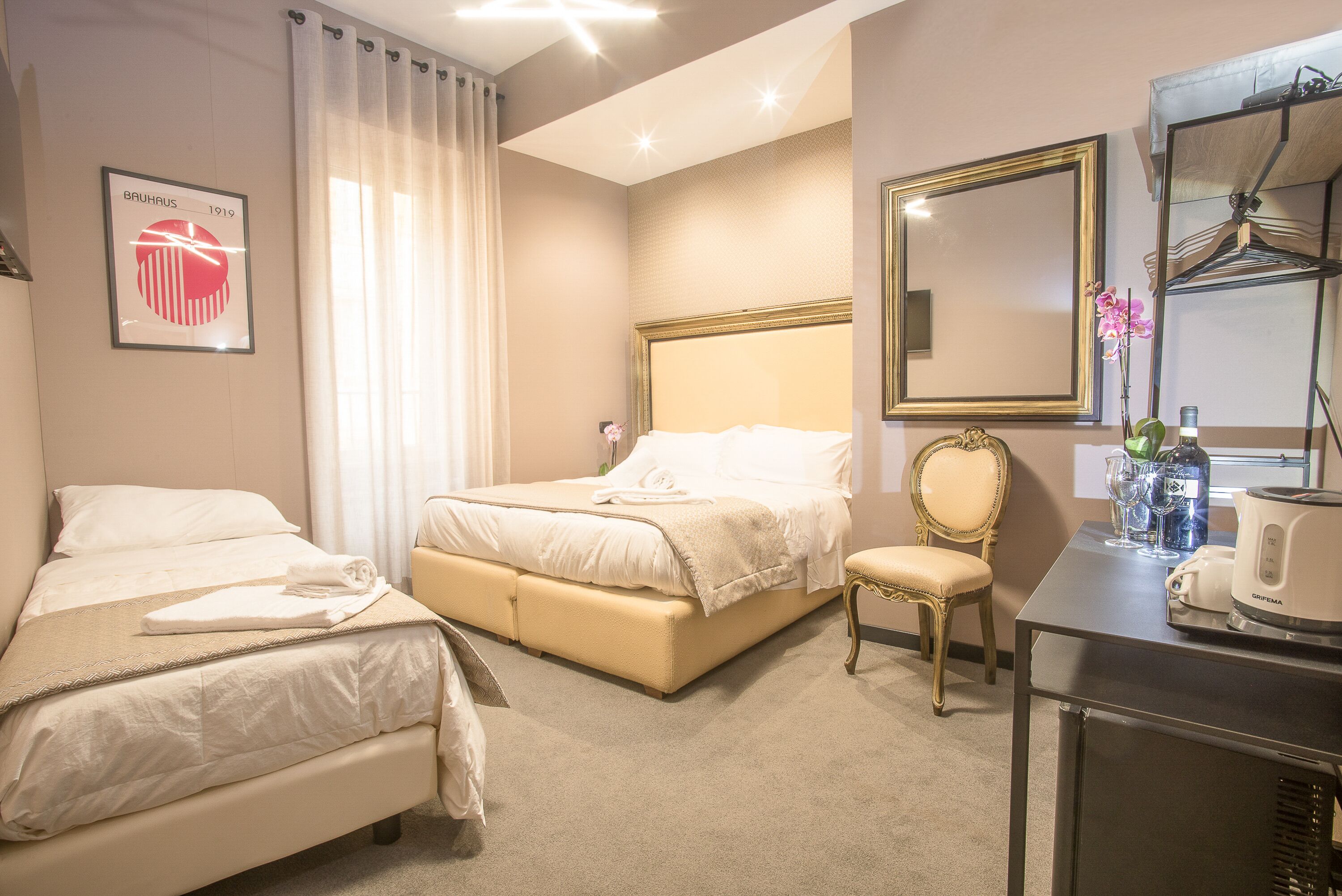 Una camera d'albergo con due letti, una sedia, una scrivania con un bollitore e uno specchio.
