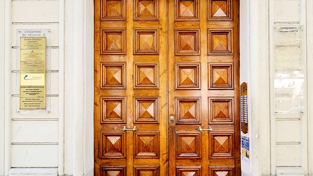 A large wooden double door with a decorative pattern, flanked by two plaques and a number sign. - Rometobe Rooms & Hospitality (Rome)