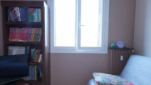 Una stanza con una libreria in legno, un divano, una finestra e un termosifone.