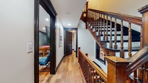 A wooden staircase with a handrail, a hallway with wooden flooring, and a door leading to a room with a pool table. - Pool Table|King Beds|0.6 miles from UofL|Downtown (Louisville)