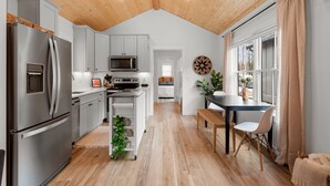 A modern kitchen with a wooden ceiling, stainless steel appliances, and a dining area with a table and chairs. - Seabrook Right as Rain | Pet Friendly, Cabin, 1BR | Sleeps 6, Fernwood (Pacific Beach)