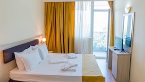 Habitación de hotel con cama, escritorio, televisión y balcón con cortinas.