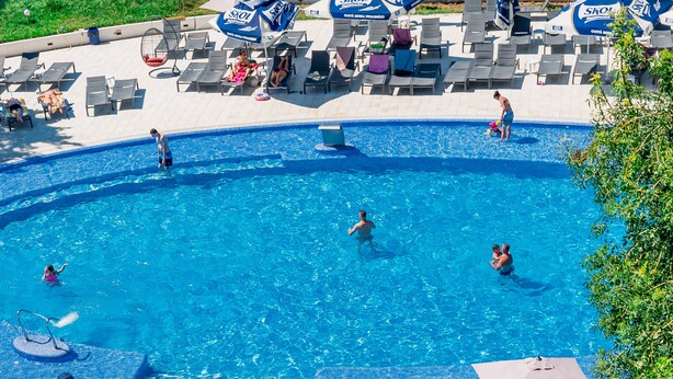 Zona de piscina con sillones de descanso y sombrillas, una piscina y un patio con mesas y sillas.