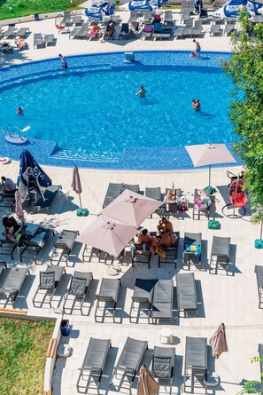 A pool area with lounge chairs and umbrellas, a swimming pool, and a patio with tables and chairs. - Apollo Hotel (Neptun)