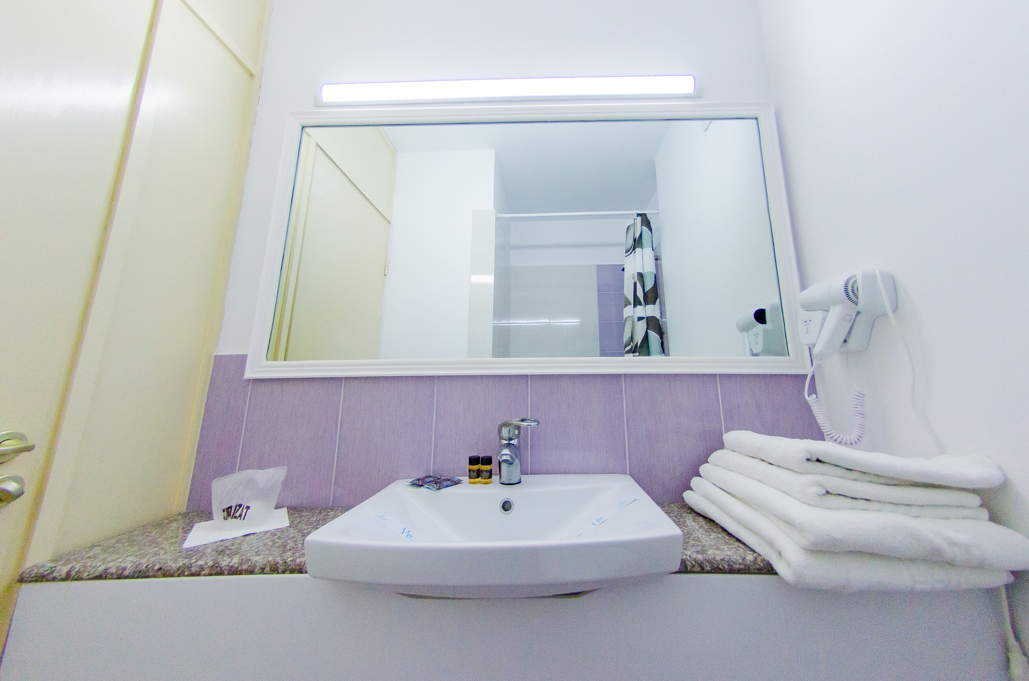 Un baño con un lavamanos blanco, un espejo y un perchero para toallas.