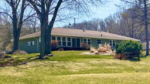 A single-story house with a sloped roof, surrounded by a well-maintained lawn and a few trees. - Golf view! (Red Wing)