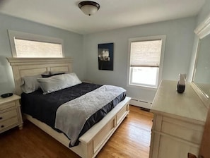 Un dormitorio con cama, mesita de noche, cómoda y ventana.
