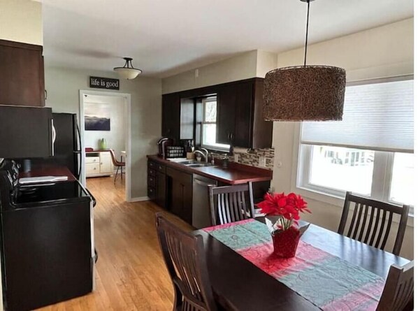 A modern kitchen with dark cabinetry, a central island, and a dining area with a table and chairs. - Golf view! (Red Wing)