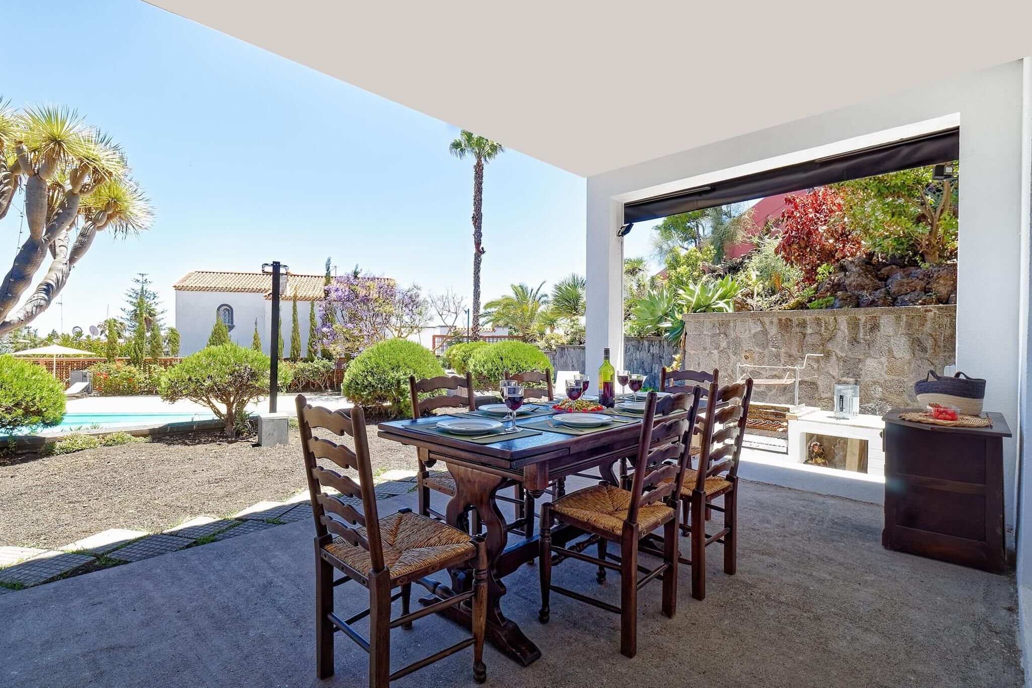 An outdoor dining area with a table set for four, surrounded by chairs, and a view of a pool and garden.
