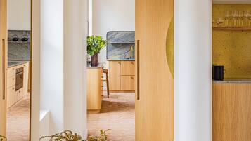Un interior moderno con zona de comedor de madera, cocina con salpicadero de mármol y un espejo grande que refleja el ambiente.