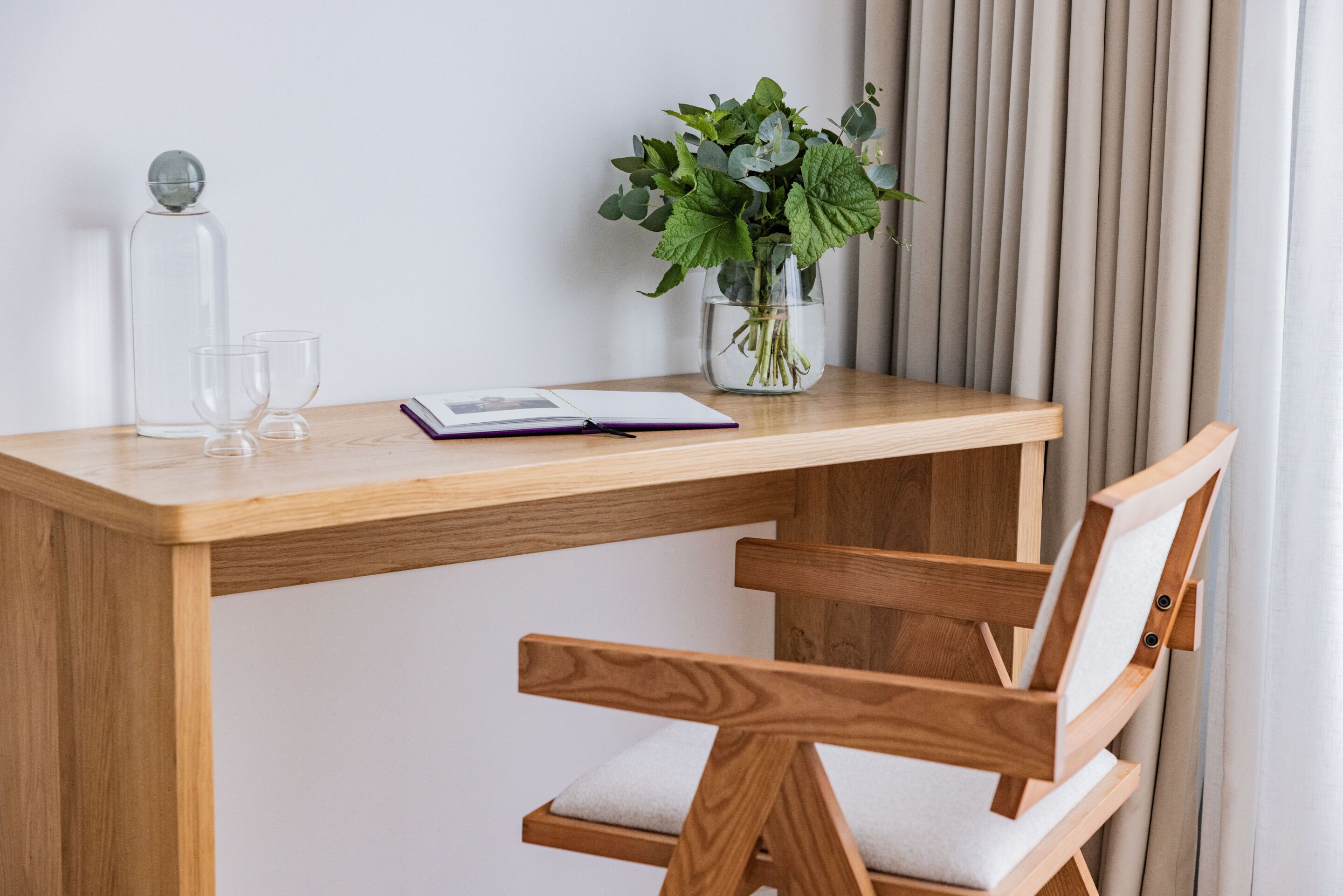 A wooden desk with a vase of green plants, two clear glasses, and a notebook.