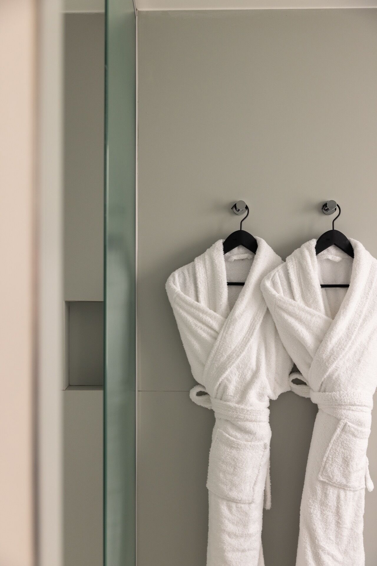 Zwei weiße Bademäntel hängen an einem Wandhaken im Badezimmer.