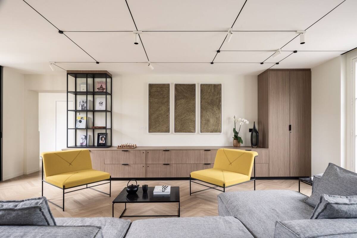 Una sala moderna con dos sillones amarillos, un sofá gris, una mesa de centro negra y una estantería con marcos de fotos.