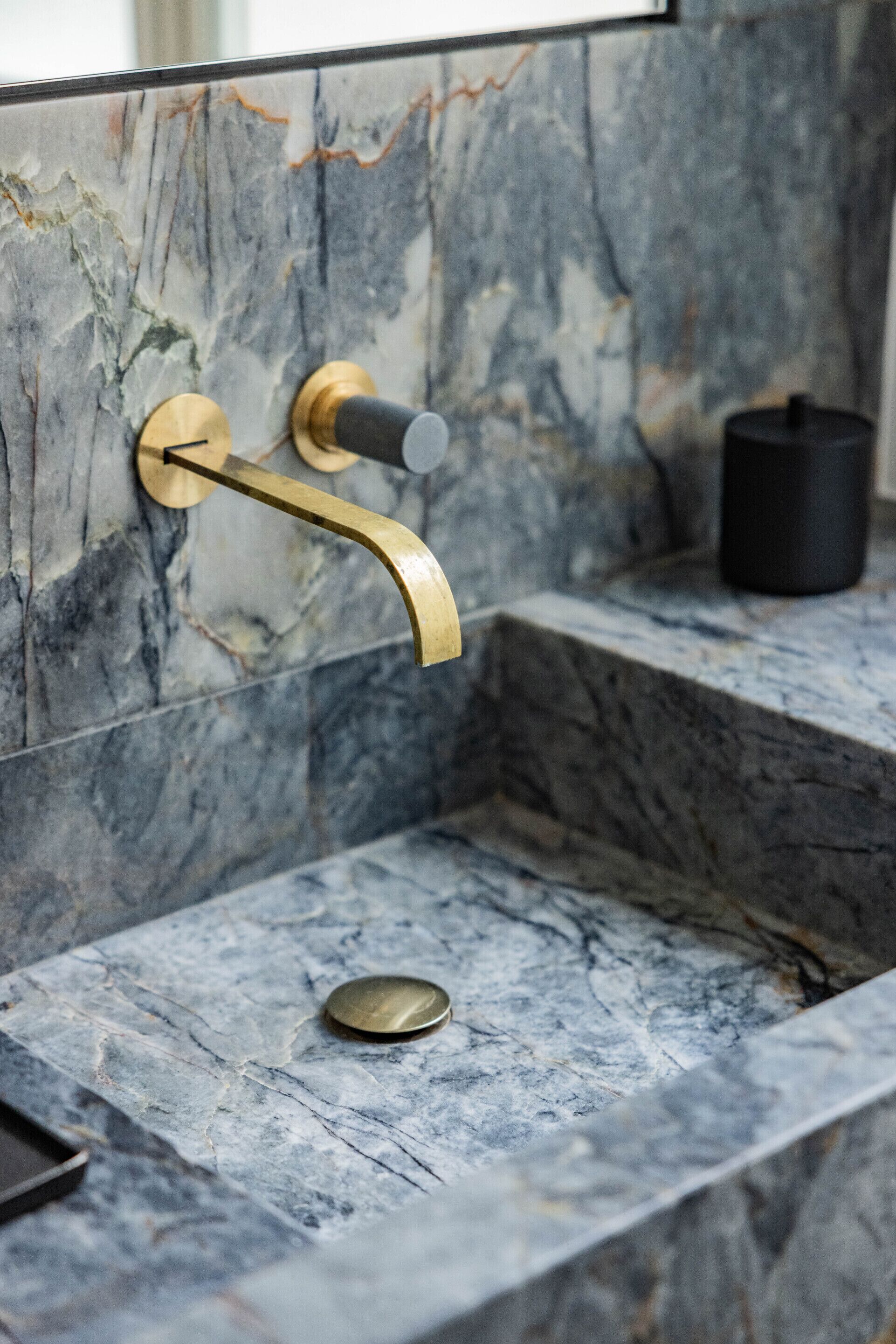 Un baño con lavamanos de mármol, grifo dorado y dispensador de jabón negro.
