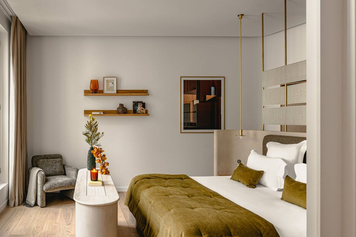 Una habitación de hotel moderna con una cama, una silla, una mesita y un estante en la pared con adornos.