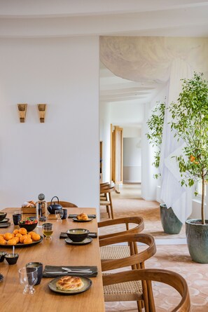 A dining area with a wooden table set for a meal, surrounded by chairs. There are potted plants and a view of a hallway with a door. - 1.75 Paris La Source (Paris)