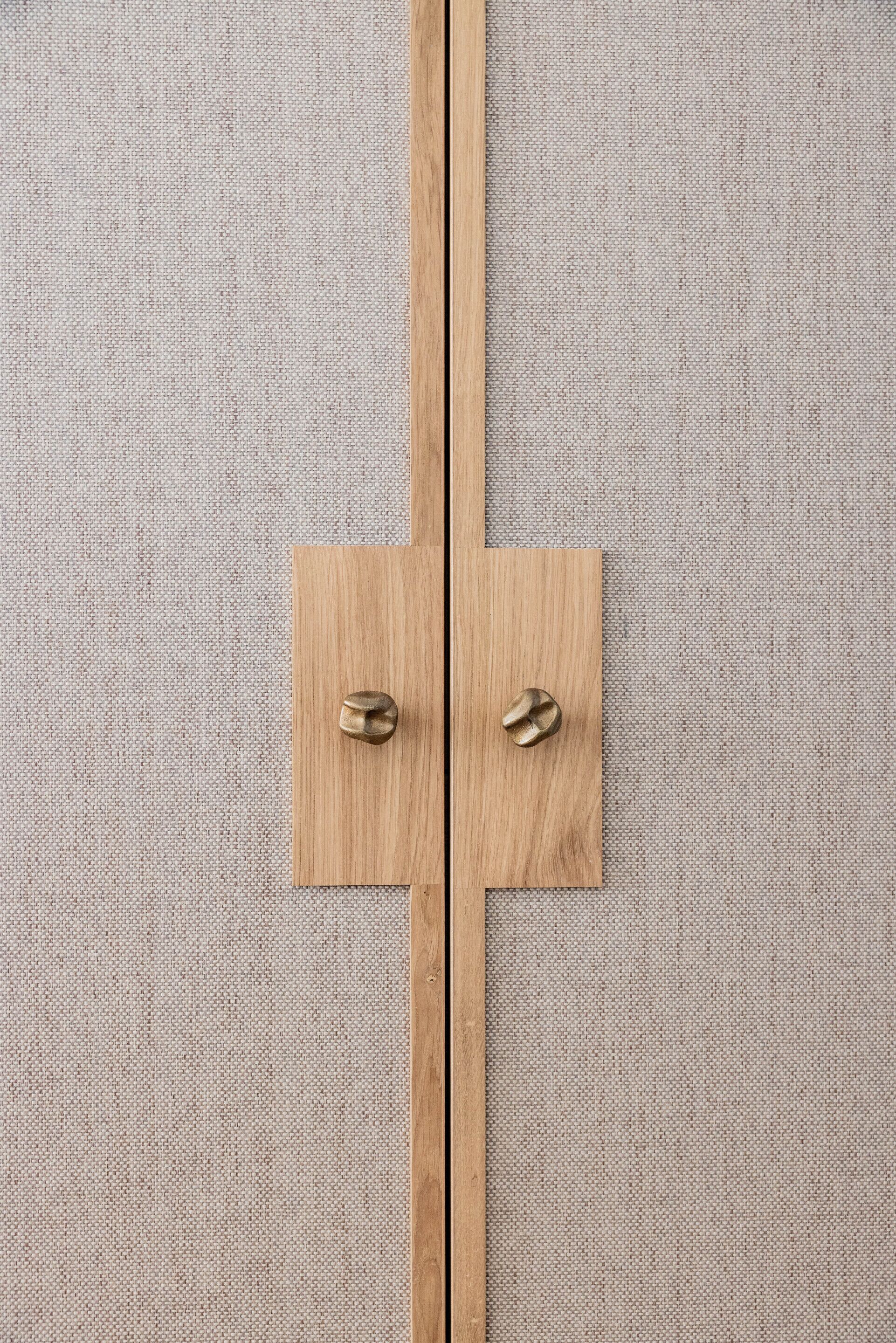 Een houten deur met twee messing klinken tegen een beige muur met structuur.