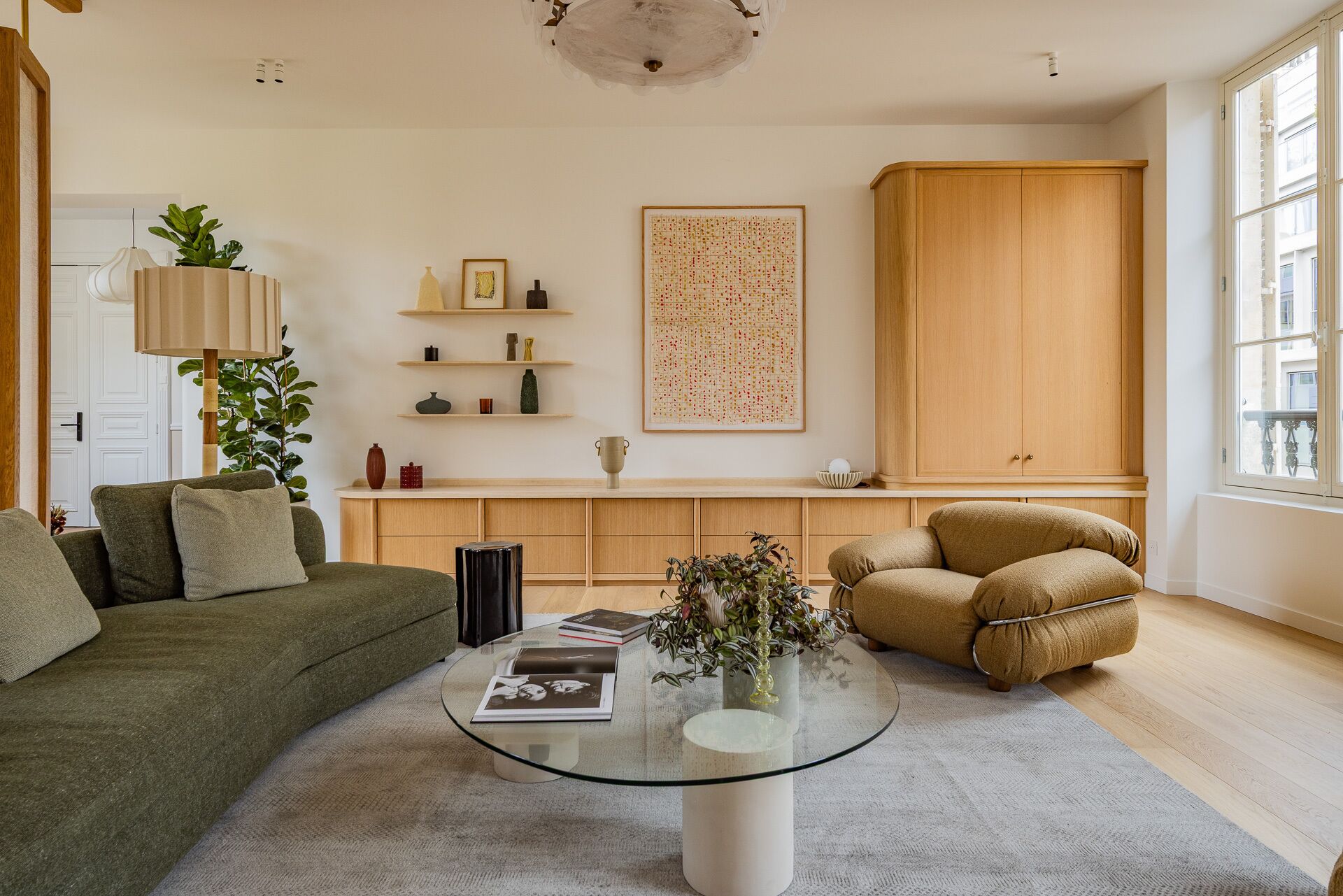 A living room with a green sofa, a brown armchair, a glass coffee table, and a wooden cabinet.