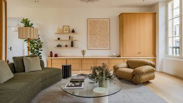 A living room with a green sofa, a brown armchair, a glass coffee table, and a wooden cabinet.